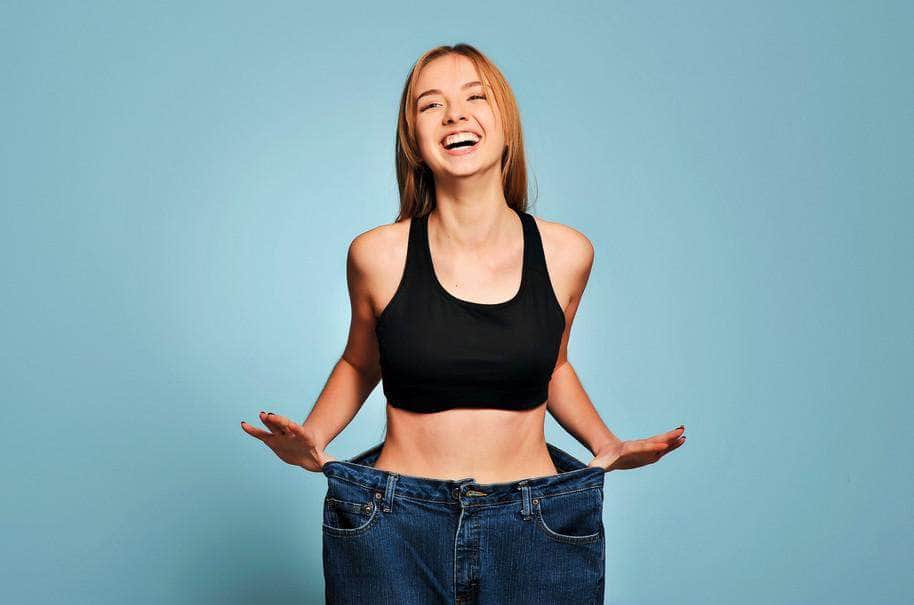 Happy woman wearing oversized jeans and smiling confidently, celebrating visible weight loss and body transformation